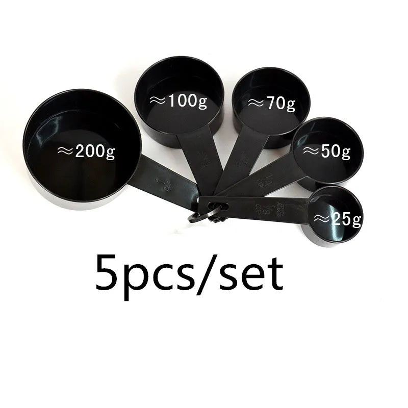 A set of five black precision kitchen measuring spoons with various capacities marked in grams.