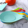 A stack of colorful silicone kitchen spatulas and spoons are displayed on a white marble surface.
