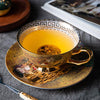 A golden bone china tea cup and saucer filled with amber tea, resting on a dark cloth.