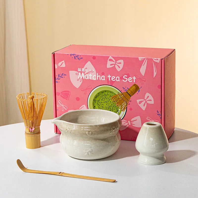 A pink box containing a Japanese matcha tea set with a ceramic bowl, whisk, and scoop on a white surface.