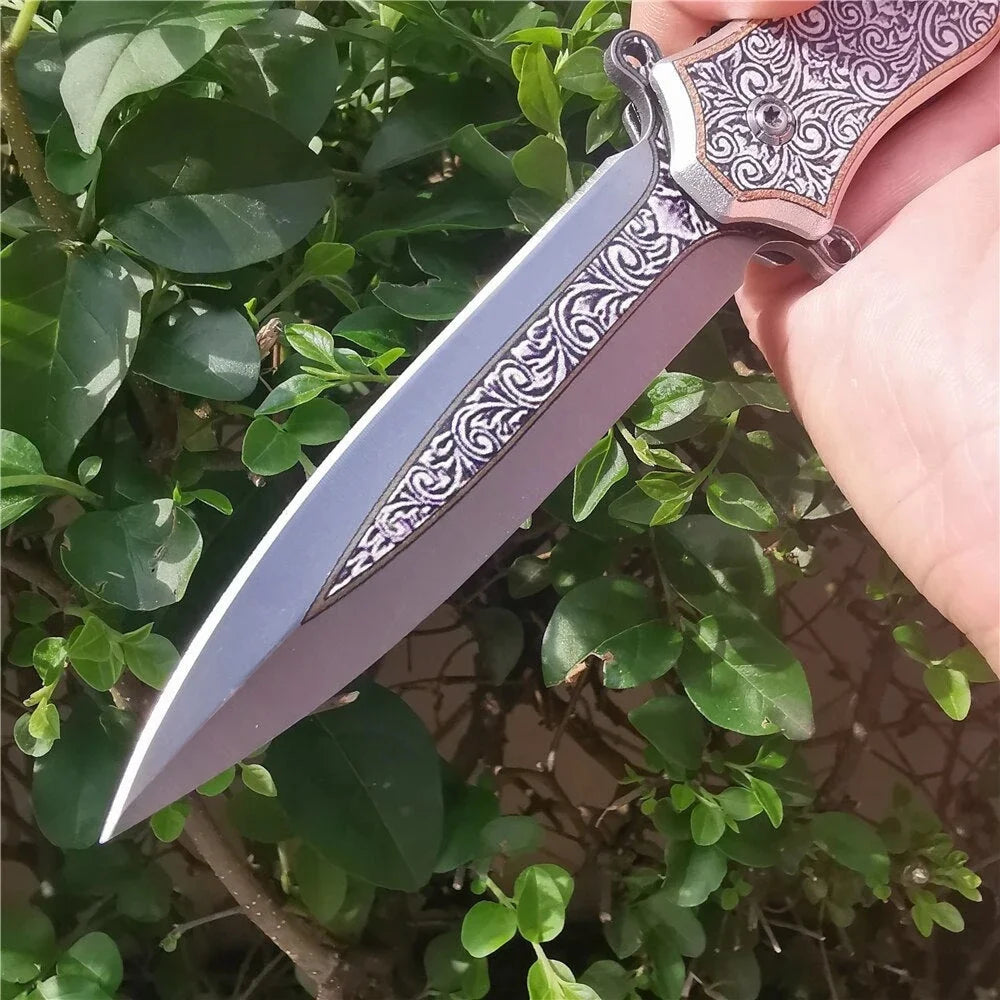A folding utility blade knife with a silver blade and patterned handle is shown against a green leafy background.