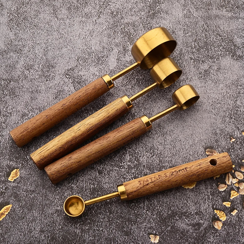 A set of four brass and wood measuring spoons for baking and bartending displayed on a gray surface.