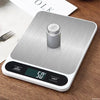 A silver digital kitchen scale is placed on a wooden surface, with a small jar of food visible.