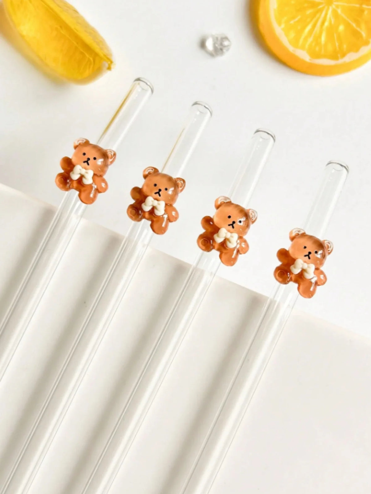 A set of reusable glass straws with small, bear-shaped silicone or wax charms on a white background.