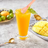 A glass of orange juice with a pink stirrer and a lime leaf garnish on a gray surface.