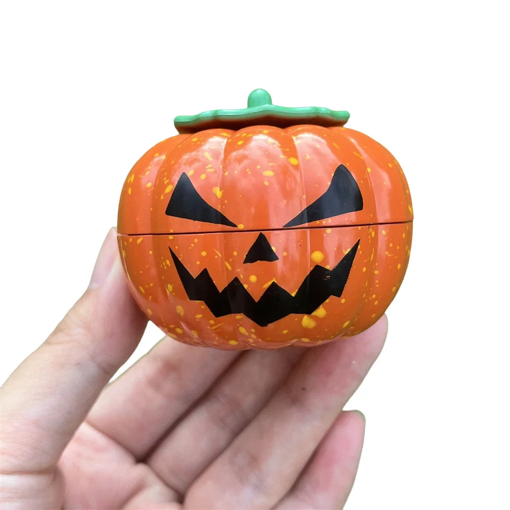 An orange pumpkin-shaped manual herb and spice grinder with a green lid is held in a hand.