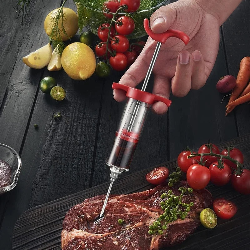 A hand holds a red meat injector kit with a syringe and various fresh ingredients like tomatoes and lemons.