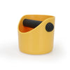 A yellow coffee knock box with a black plunger, designed for crushing espresso grounds.