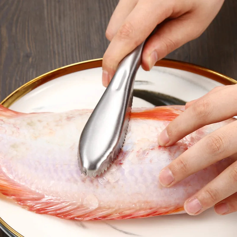 Une main utilise un détartrant en acier inoxydable pour nettoyer la peau d'un poisson cru sur une assiette blanche.