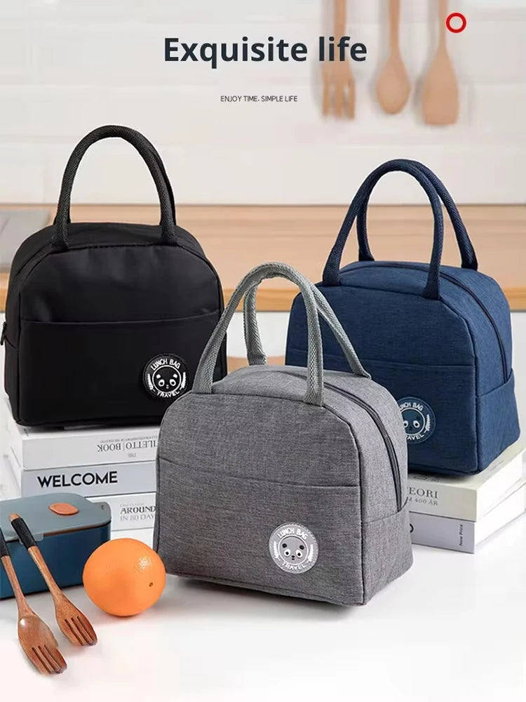 Three insulated bento lunch bags in black, navy blue, and gray are displayed with wooden utensils.