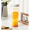 A clear glass jar filled with orange-colored cold brew coffee, sitting on a white marble surface.