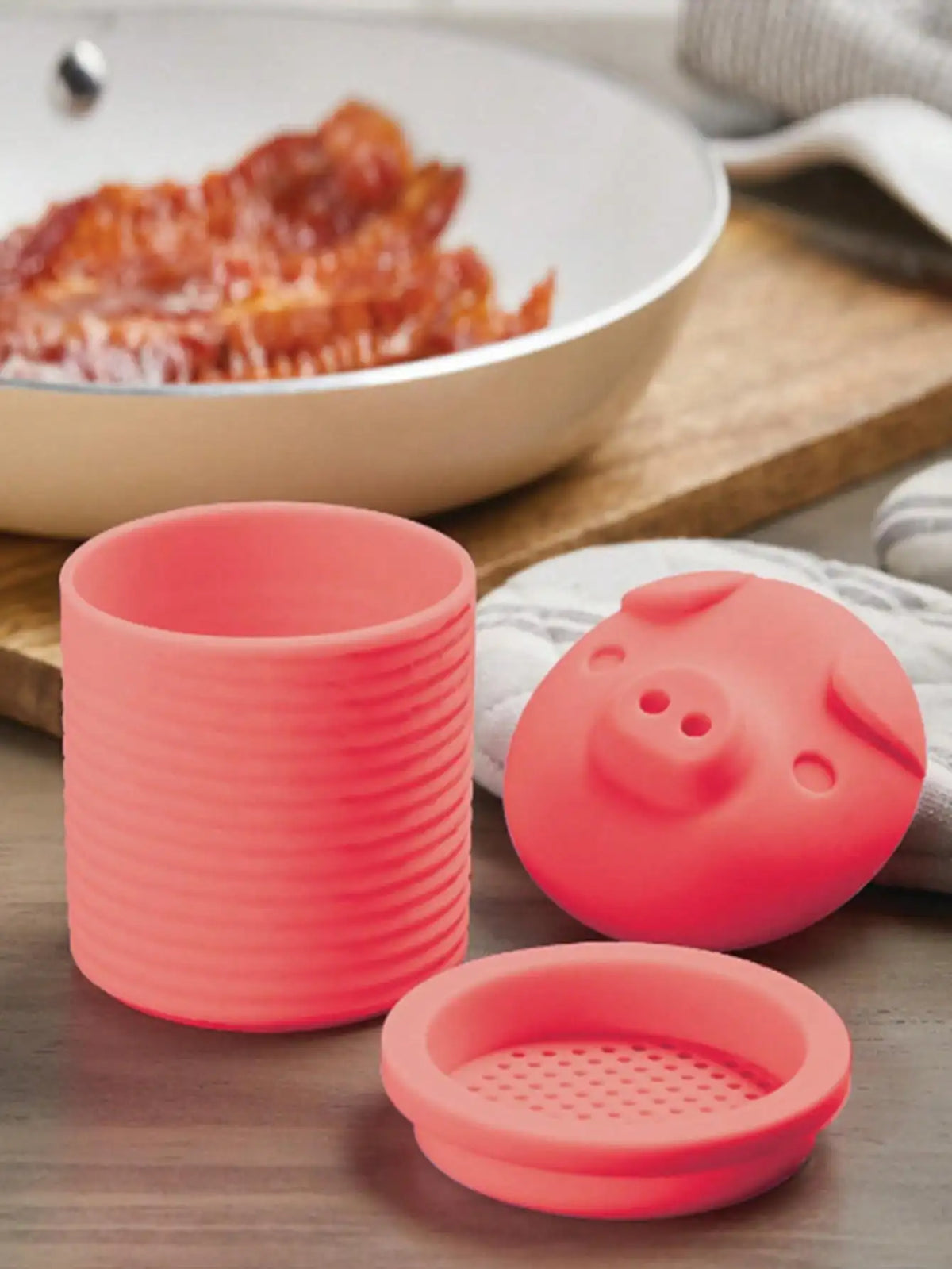 A pink silicone grease collector with multiple openings rests on a wooden surface next to a bowl of oil.