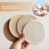 A hand holds a set of four woven absorbent coasters made from thick, soft, coarse cotton rope.