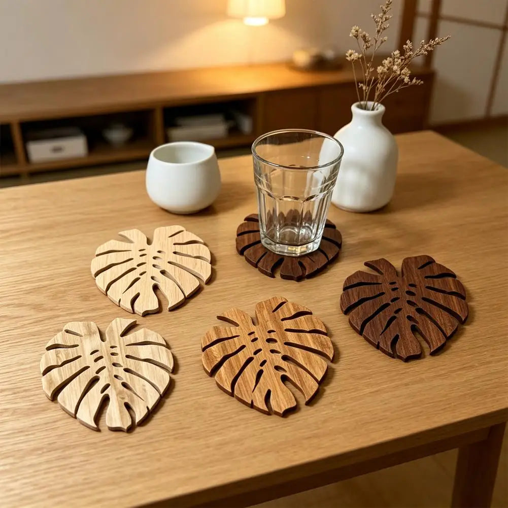 Ein Set aus fünf Holzscheiben mit tropischen Blättern auf einem hellen Holztisch mit Glas und einer weißen Keramiktasse.