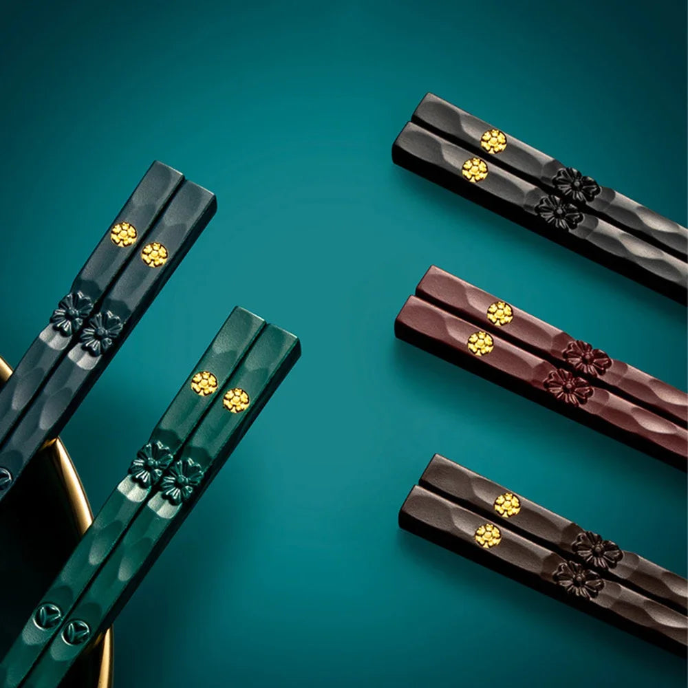 A set of five pairs of reusable food-grade metal chopsticks in dark green and brown tones are displayed on a teal surface.