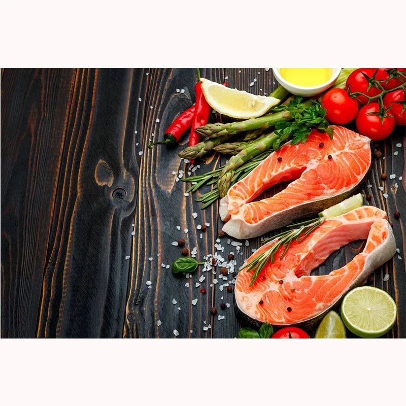A sliced salmon fillet is displayed on a dark wooden board with lemon slices, chili peppers, and herbs.