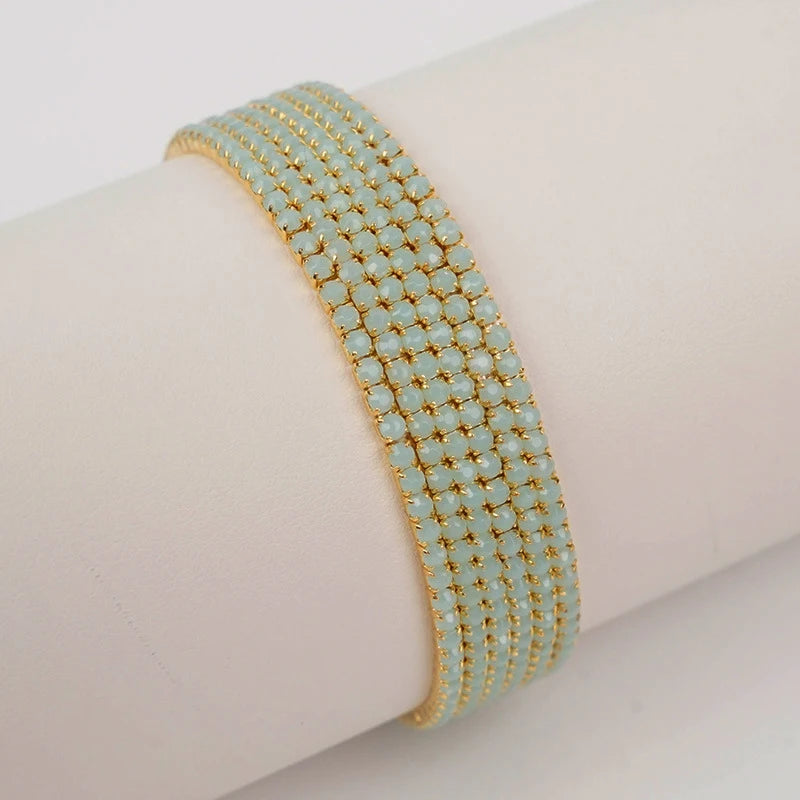 A stack of gold acrylic elastic bracelets with small light blue stones worn on a wrist.