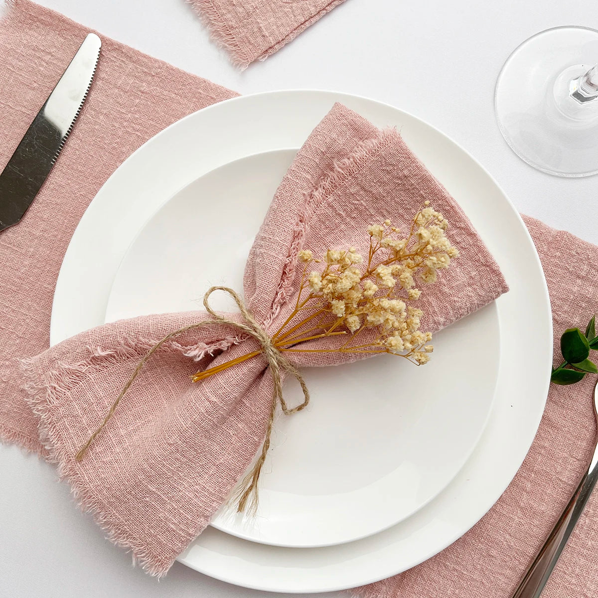 Una pila de servilletas de algodón reutilizables rosadas atadas con hilo sobre un plato blanco y una servilleta de lino.