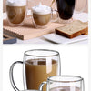 A set of clear double-wall glass drinking cups filled with hot beverage and topped with foam, next to toast.