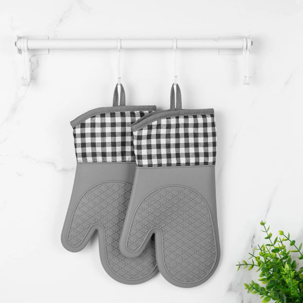Gray silicone oven mitts with checkered quilted liners hanging on a white rack.