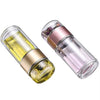 A clear glass tea infuser with a pink and gold colored top section is shown.