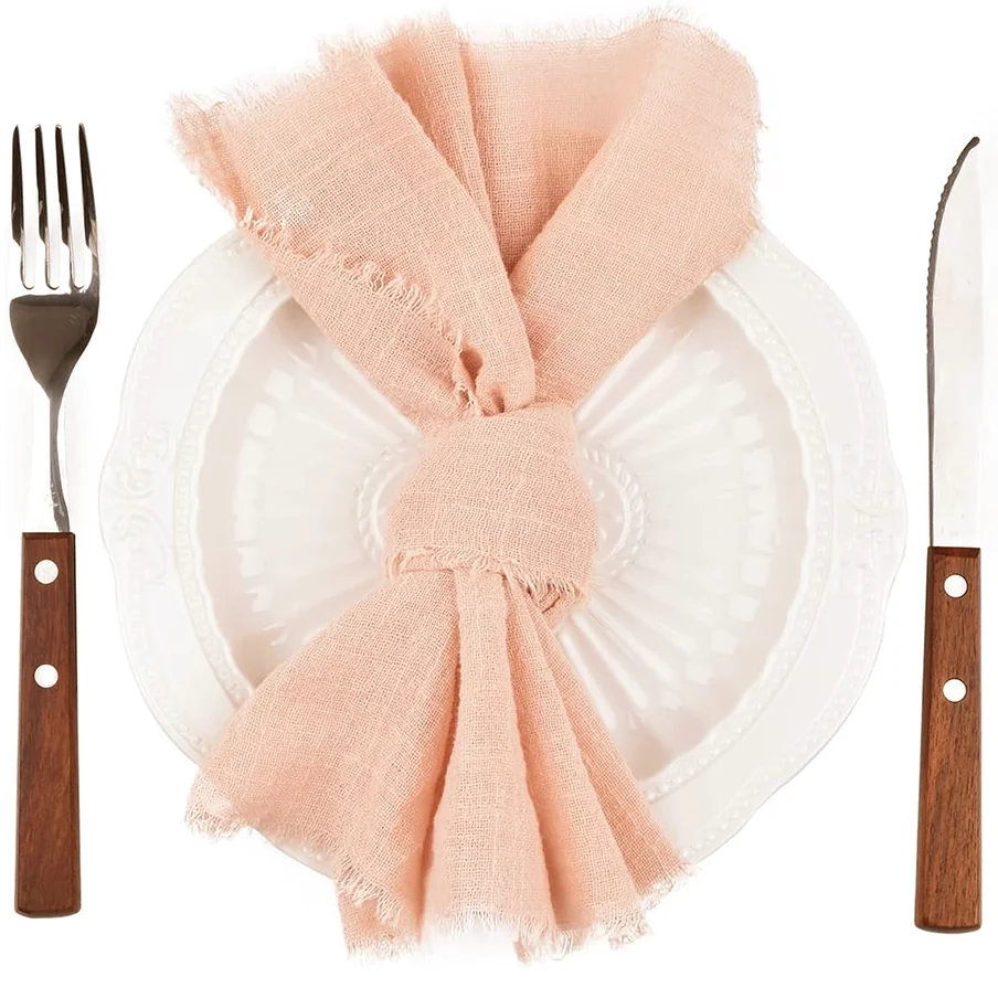 Servilleta de algodón rosa atada en un lazo colocada sobre un plato blanco junto a un tenedor y cuchillo.