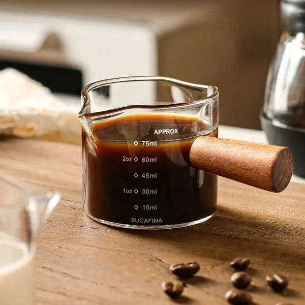 Ein Glasmessbecher mit dunkler Flüssigkeit, beschriftet Sucafina und ca. 75ml, auf einer Holzoberfläche.