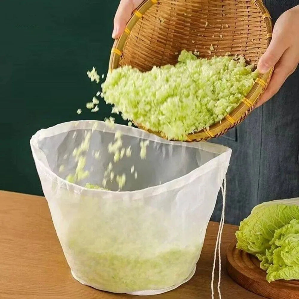 A hand is pouring finely chopped green herbs or vegetables from a woven basket into a white reusable food filter bag.