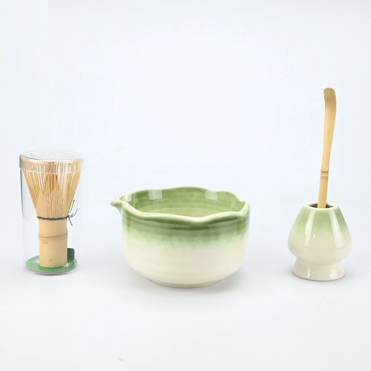 A set of light green ceramic matcha bowls and bamboo brushes displayed on a white background.