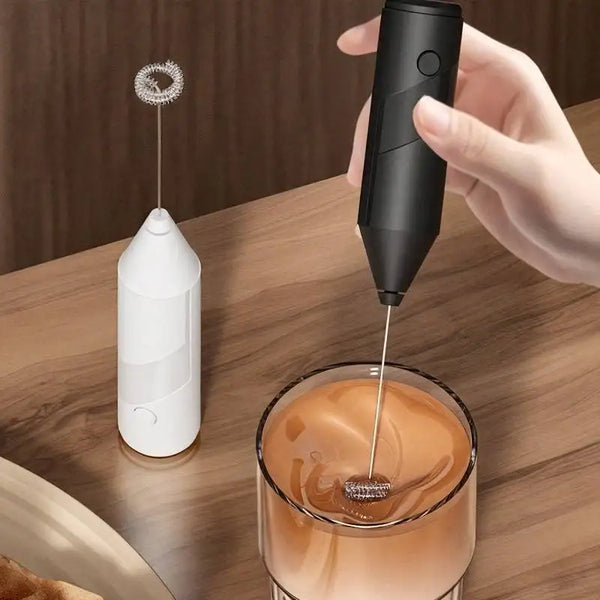 Eine Hand hält einen schwarzen Handmixer für Milch, der in einen Orangensaft gießt.