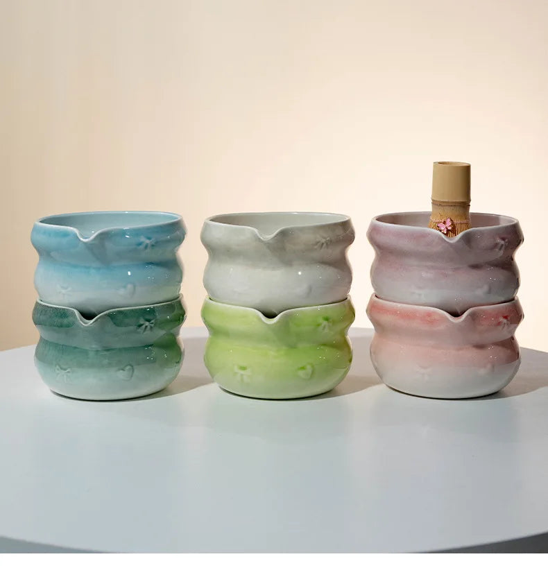 A set of three stacked ceramic bowls in shades of blue, green, and pink with a bamboo lid.