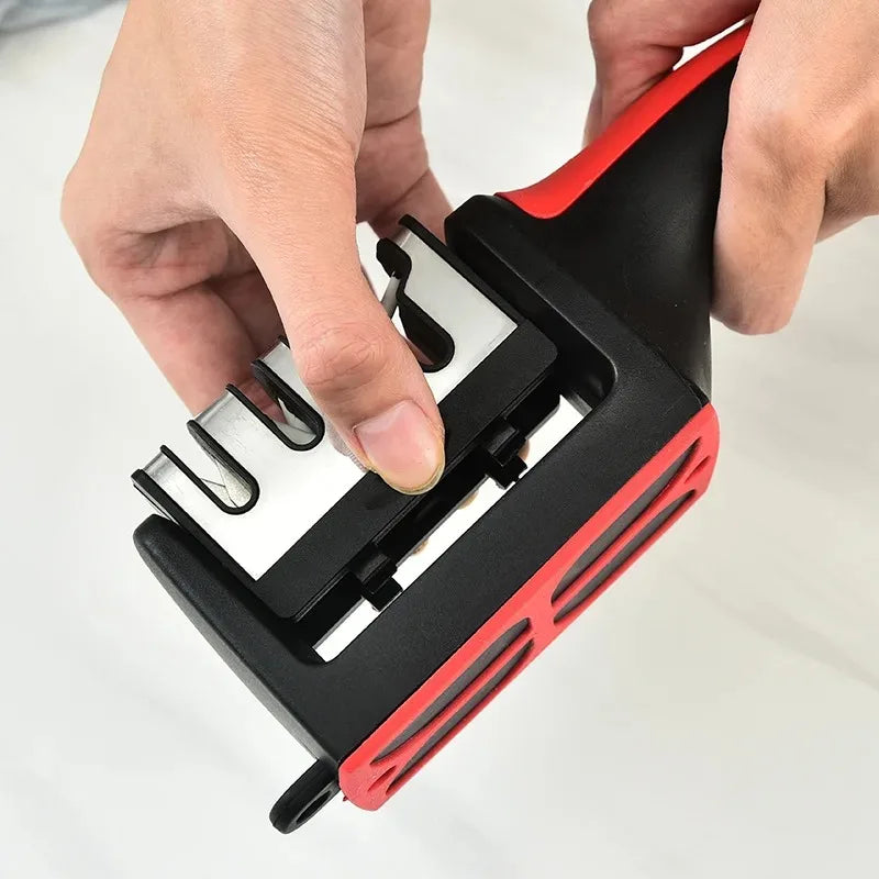 A hand is holding and operating a black and red 4-stage handheld knife sharpener.