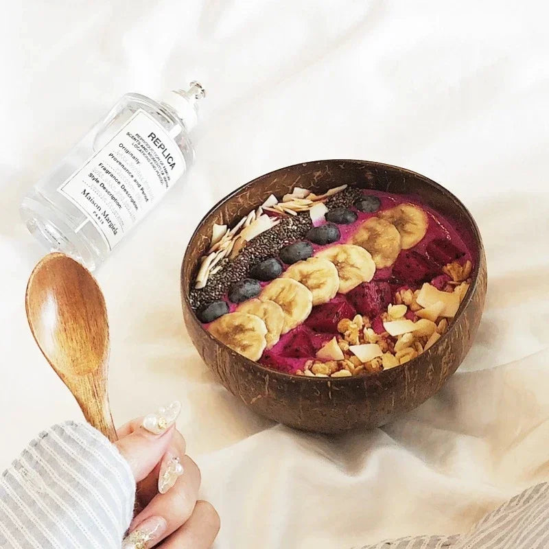 A wooden spoon is shown next to a glass bottle of replica oil and a bowl filled with a purple fruit salad.