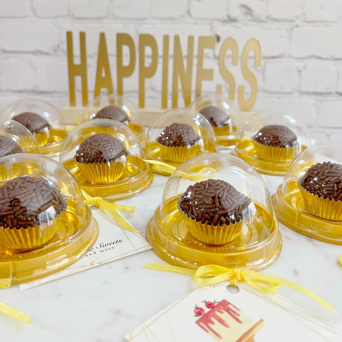 A collection of mini transparent cake boxes filled with chocolate cupcakes arranged on a white surface.