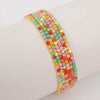 A stack of colorful acrylic elastic bracelets in various shades of pink, orange, green, and yellow on a white wrist.