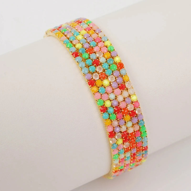 A stack of colorful acrylic elastic bracelets in various shades of pink, orange, green, and yellow on a white wrist.