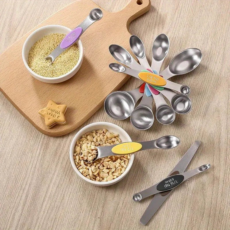 A set of nine stainless steel measuring spoons and a magnetic suction tool are displayed on a wooden cutting board.