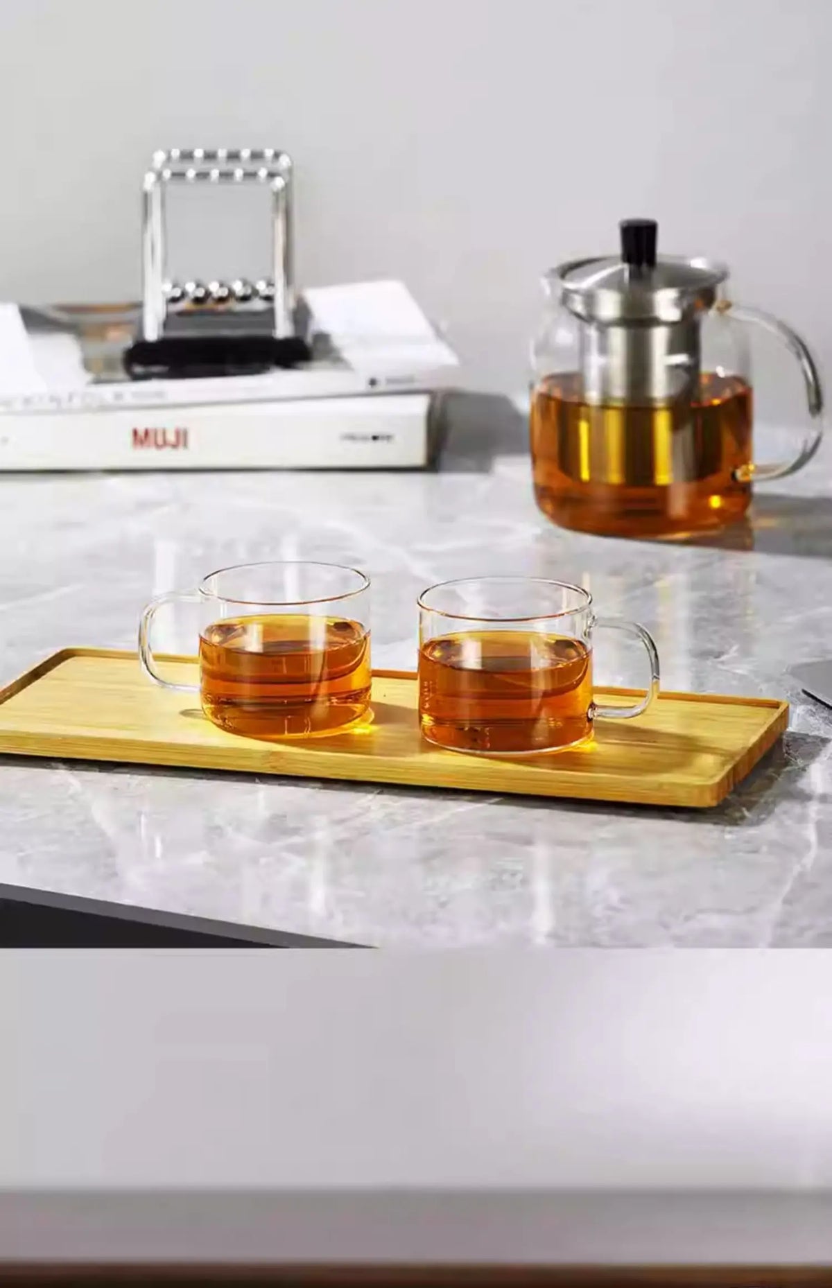 A set of durable borosilicate glass tea cups and a glass teapot are displayed on a marble surface.