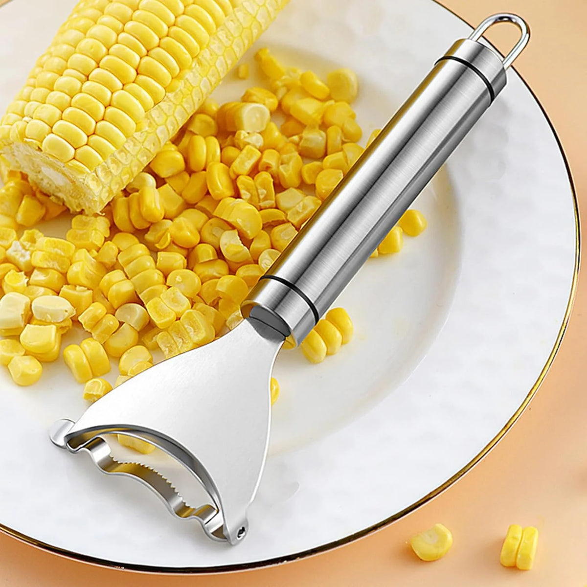 A stainless steel corn planer peeler is shown with corn kernels on a white plate.