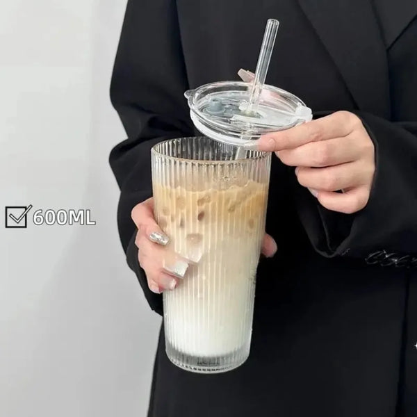 Eine Hand hält ein Glas Eiskaffee oder Milchgetränk mit klappender Deckel und Strohhalm vor einem schwarzen Sakko.