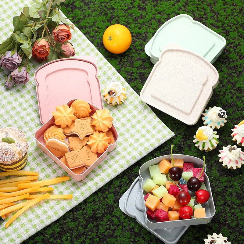 A collection of reusable pink and light green microwave sandwich containers, lids, and food items arranged on a green surface