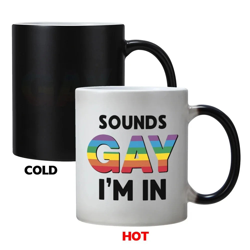 A white ceramic mug with black handle displaying the text Sounds Gay I'm In, shown next to a black version labeled cold and h