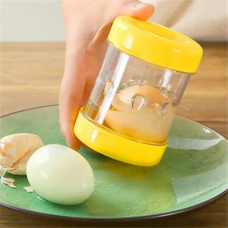Une main utilise un outil à manivelle jaune pour retirer la coquille d'un œuf cru dans un récipient transparent.