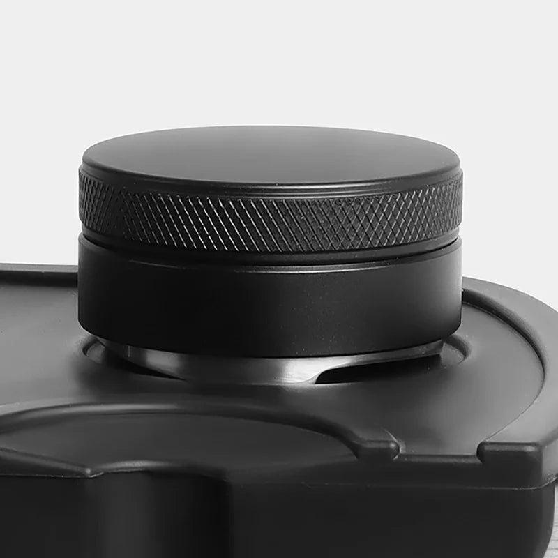 A black precision espresso distribution tool with a threaded cap resting on its base.
