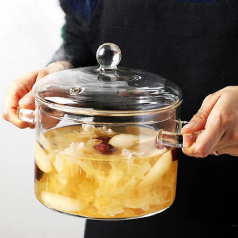 Una persona sostiene una olla de vidrio transparente llena de fruta amarilla y líquido para cocinar.