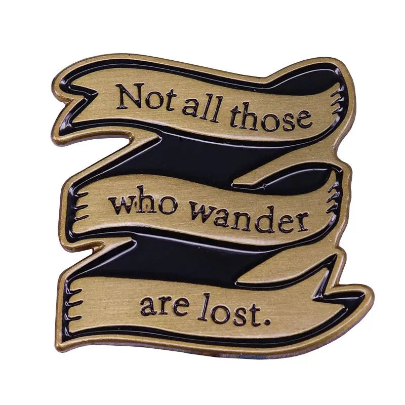 A gold-toned enamel pin featuring a black ribbon design with the text Not all those who wander are lost.
