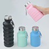 A hand holds a pink collapsible silicone water bottle next to stacked black and blue versions.