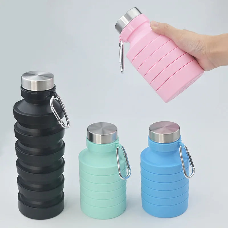 A hand holds a pink collapsible silicone water bottle next to stacked black and blue versions.