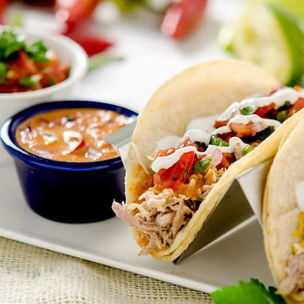 A hand-held taco is shown inside a soft tortilla, served with salsa and garnishes on a white plate.