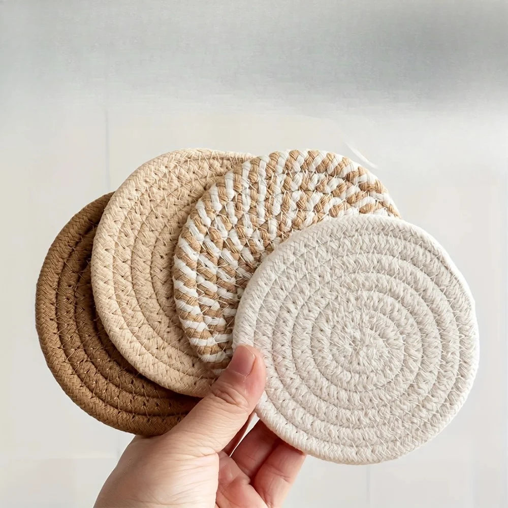 A hand holds a set of four woven absorbent coasters in natural beige and cream tones.